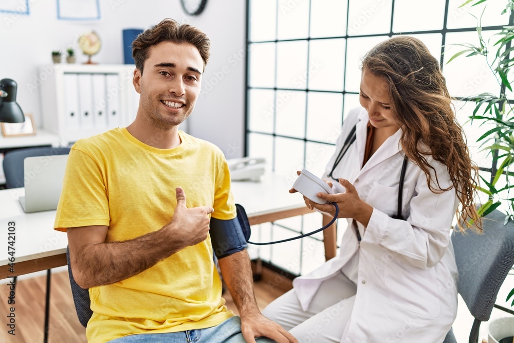 Young doctor woman checking blood pressure on patient smiling happy pointing with hand and finger