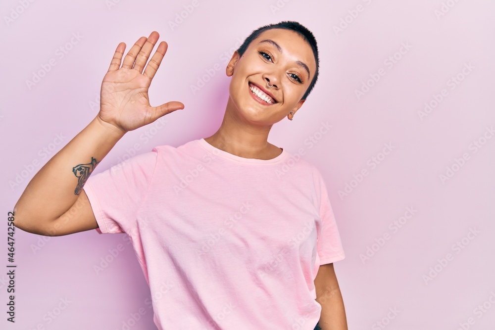 Beautiful hispanic woman with short hair wearing casual pink t shirt waiving saying hello happy and smiling, friendly welcome gesture Beautiful hispanic woman with short hair wearing casual pink t shirt waiving saying hello happy and smiling, friendly welcome gesture