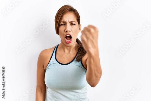 Young latin woman wearing sporty clothes over isolated background angry and mad raising fist frustrated and furious while shouting with anger. rage and aggressive concept.
