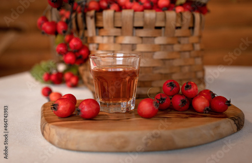 Fototapeta A small shot glass with hawthorn tincture on the background of a wicker brown basket and scattered berries of ripe red hawthorn, a medicinal drink