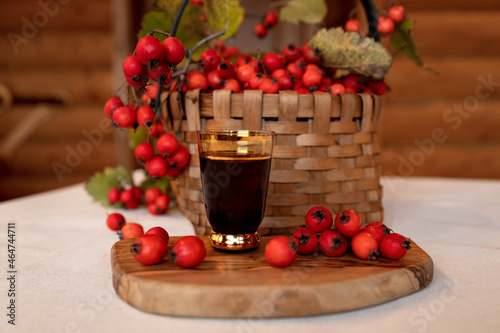 A wicker basket full of red ripe hawthorn berries, next to a glass with a tincture of hawthorn. Medicinal drinks, folk medicine.