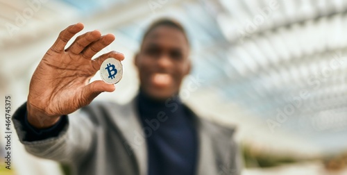 Young african american man smiling happy holding bitcoin at the city