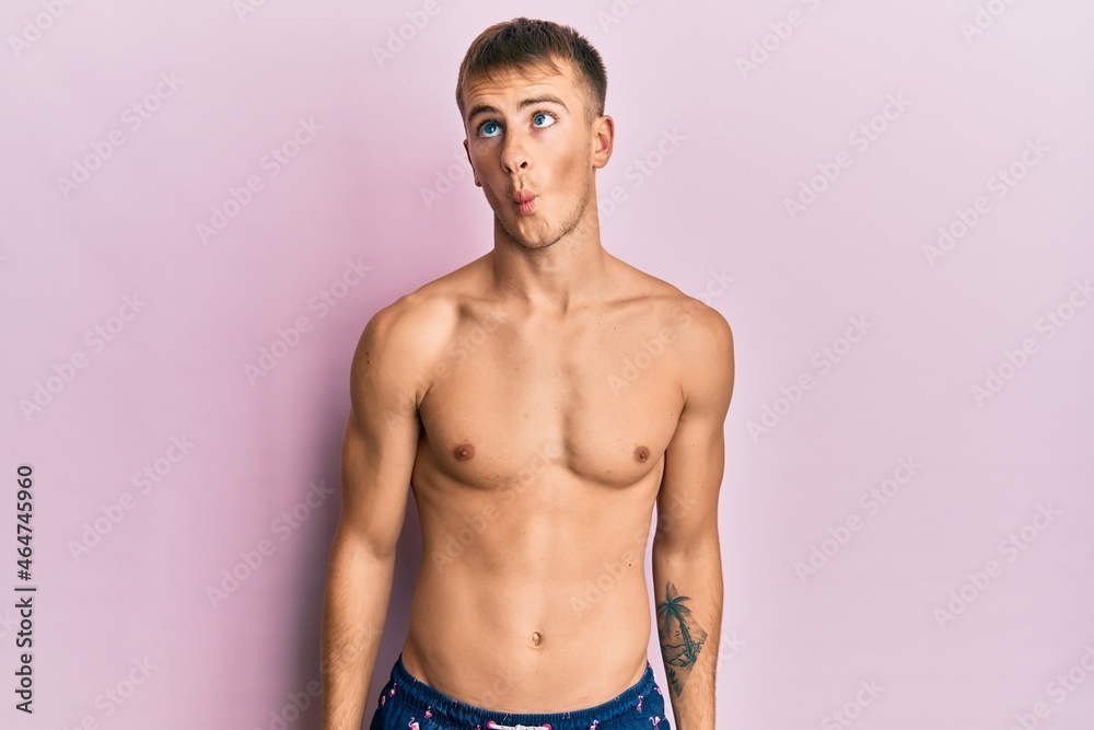 Young caucasian man wearing swimwear making fish face with lips, crazy and comical gesture. funny expression.
