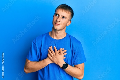 Young caucasian man wearing casual blue t shirt smiling with hands on chest with closed eyes and grateful gesture on face. health concept.