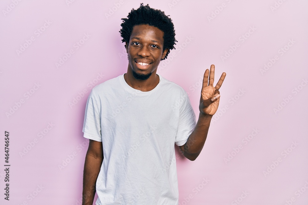 Young african american man wearing casual white t shirt showing and pointing up with fingers number three while smiling confident and happy. Young african american man wearing casual white t shirt showing and pointing up with fingers number three while smiling confident and happy.