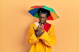 Young african american man wearing yellow raincoat suffering pain on hands and fingers, arthritis inflammation