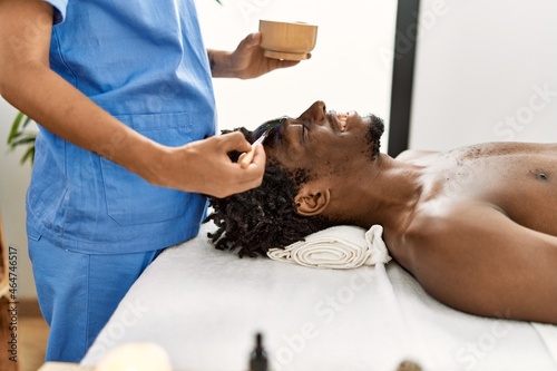 African american man reciving facial treatment at beauty center.