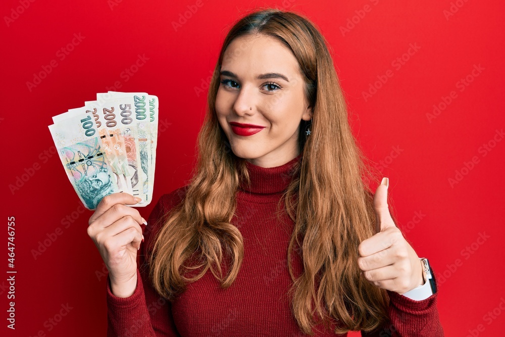 Young blonde woman holding czech koruna banknotes smiling happy and positive, thumb up doing excellent and approval sign Young blonde woman holding czech koruna banknotes smiling happy and positive, thumb up doing excellent and approval sign