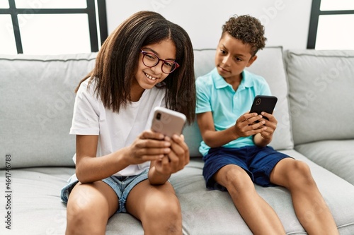 Brother and sister using smartphone sitting on sofa at home