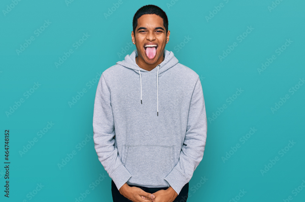 Young handsome hispanic man wearing casual sweatshirt sticking tongue out happy with funny expression. emotion concept. Young handsome hispanic man wearing casual sweatshirt sticking tongue out happy with funny expression. emotion concept.
