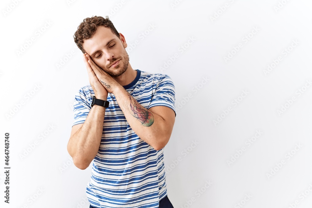 Handsome young man standing over isolated background sleeping tired dreaming and posing with hands together while smiling with closed eyes. Handsome young man standing over isolated background sleeping tired dreaming and posing with hands together while smiling with closed eyes.