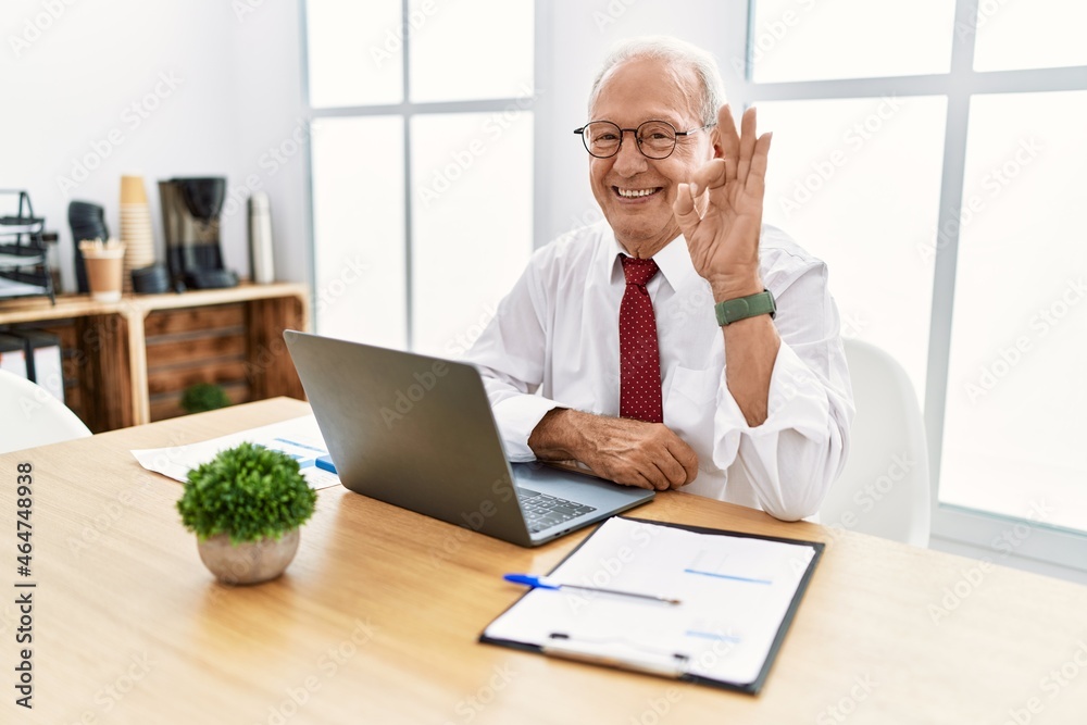 Senior man working at the office using computer laptop smiling positive doing ok sign with hand and fingers. successful expression. Senior man working at the office using computer laptop smiling positive doing ok sign with hand and fingers. successful expression.