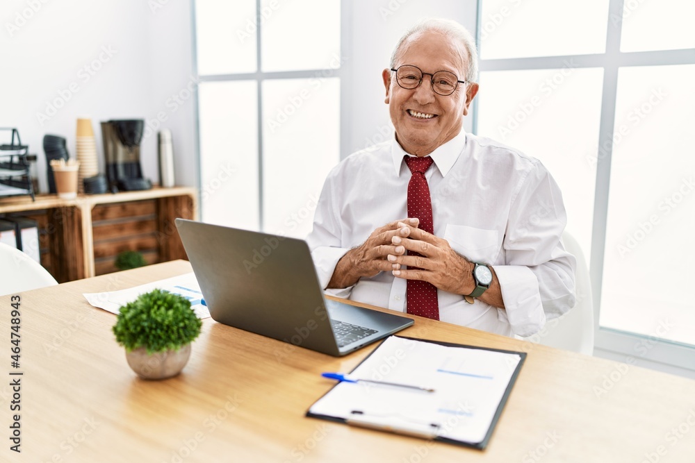 Senior man working at the office using computer laptop hands together and fingers crossed smiling relaxed and cheerful. success and optimistic Senior man working at the office using computer laptop hands together and fingers crossed smiling relaxed and cheerful. success and optimistic