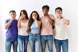 Group of young people standing together over isolated background shocked covering mouth with hands for mistake. secret concept.