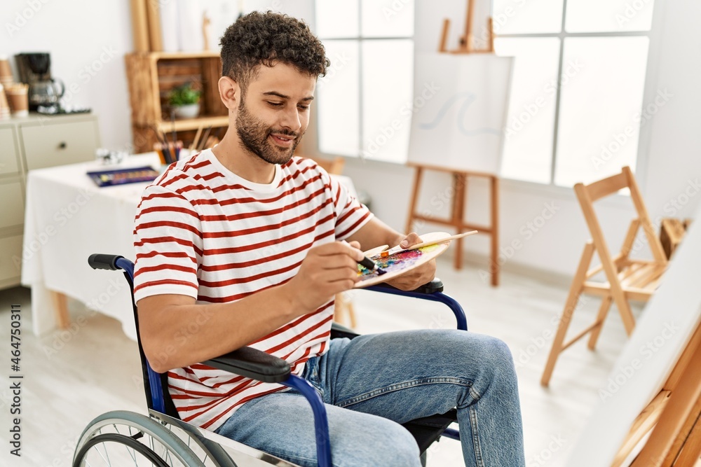 Young arab disabled artist man drawing sitting on wheelchair at art studio.