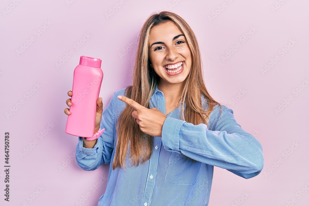 Beautiful hispanic woman holding shampoo bottle smiling happy pointing with hand and finger Beautiful hispanic woman holding shampoo bottle smiling happy pointing with hand and finger