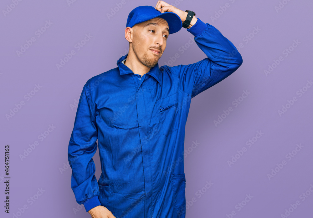 Bald man with beard wearing builder jumpsuit uniform smiling confident touching hair with hand up gesture, posing attractive and fashionable