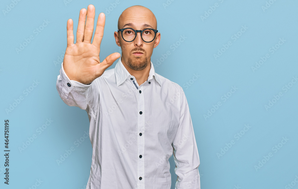 Bald man with beard wearing business shirt and glasses doing stop sing with palm of the hand. warning expression with negative and serious gesture on the face. Bald man with beard wearing business shirt and glasses doing stop sing with palm of the hand. warning expression with negative and serious gesture on the face.