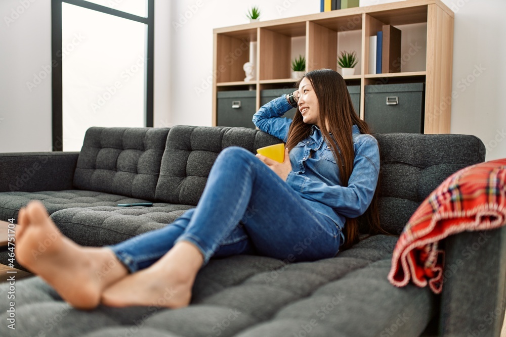Young chinese girl drinking coffee lying on the sofa at home.