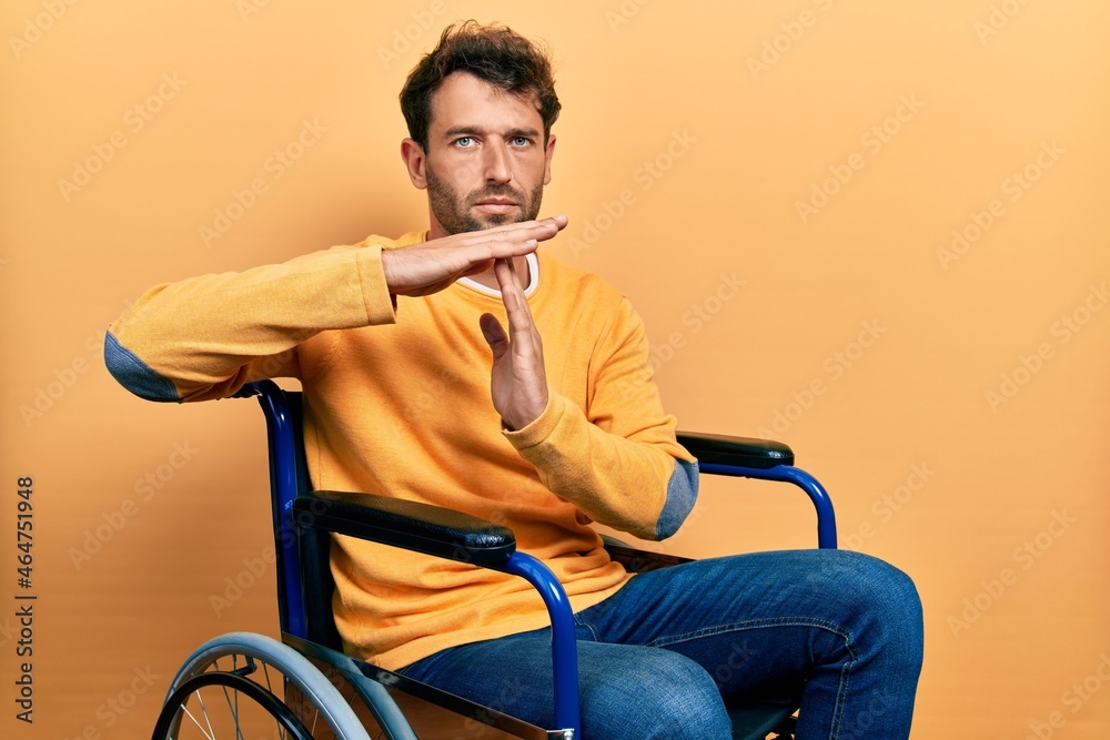 Handsome man with beard sitting on wheelchair doing time out gesture with hands, frustrated and serious face Handsome man with beard sitting on wheelchair doing time out gesture with hands, frustrated and serious face