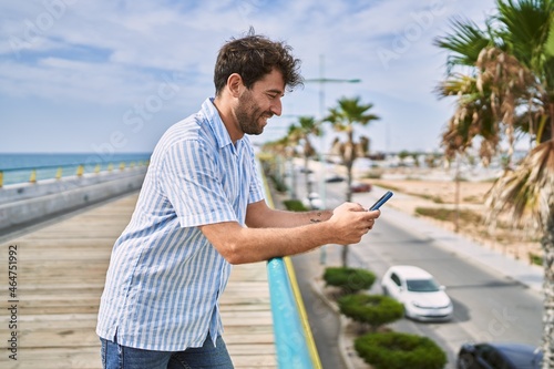 Young hispanic man smiling happy using smartphone at the promenade.