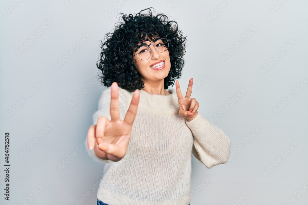 Young middle east woman wearing casual white tshirt smiling looking to the camera showing fingers doing victory sign. number two. Young middle east woman wearing casual white tshirt smiling looking to the camera showing fingers doing victory sign. number two.
