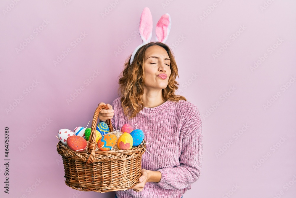 Young caucasian woman wearing cute easter bunny ears holding colored egg looking at the camera blowing a kiss being lovely and sexy. love expression.