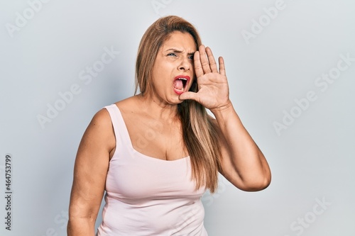 Middle age hispanic woman wearing casual style with sleeveless shirt shouting and screaming loud to side with hand on mouth. communication concept.