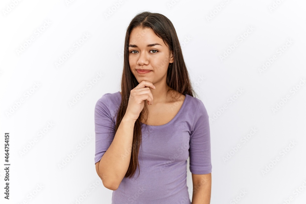 Young brunette woman standing by isolated background looking confident at the camera with smile with crossed arms and hand raised on chin. thinking positive. Young brunette woman standing by isolated background looking confident at the camera with smile with crossed arms and hand raised on chin. thinking positive.