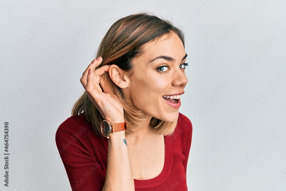 Young caucasian blonde woman wearing casual jumper smiling with hand over ear listening and hearing to rumor or gossip. deafness concept. Young caucasian blonde woman wearing casual jumper smiling with hand over ear listening and hearing to rumor or gossip. deafness concept.