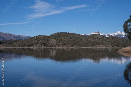 The lake in a sunny morning. Panorama view of the forest, mountain, cliffs, lake and the perfect reflection of the sky in the blue water.