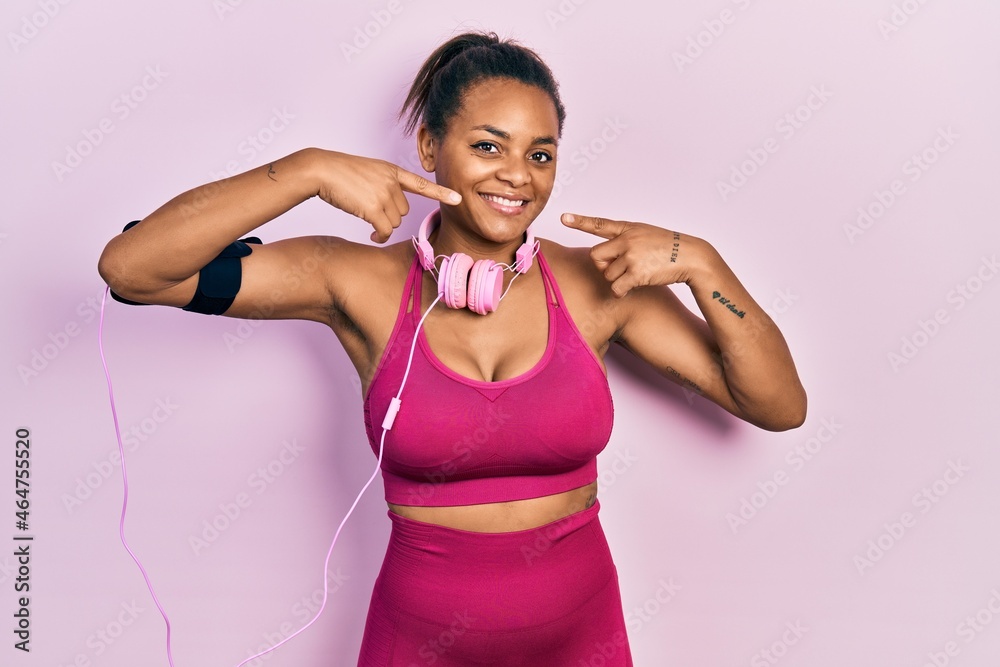 Young african american girl wearing gym clothes and using headphones smiling cheerful showing and pointing with fingers teeth and mouth. dental health concept.