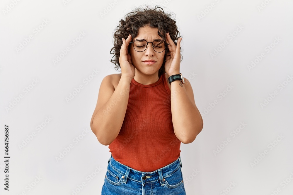 Young hispanic woman wearing glasses standing over isolated background with hand on head, headache because stress. suffering migraine. Young hispanic woman wearing glasses standing over isolated background with hand on head, headache because stress. suffering migraine.