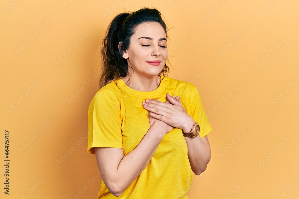 Young hispanic woman wearing casual clothes smiling with hands on chest, eyes closed with grateful gesture on face. health concept. Young hispanic woman wearing casual clothes smiling with hands on chest, eyes closed with grateful gesture on face. health concept.