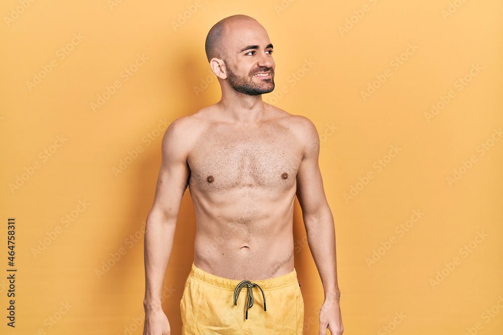 Young bald man wearing swimwear looking away to side with smile on face, natural expression. laughing confident.
