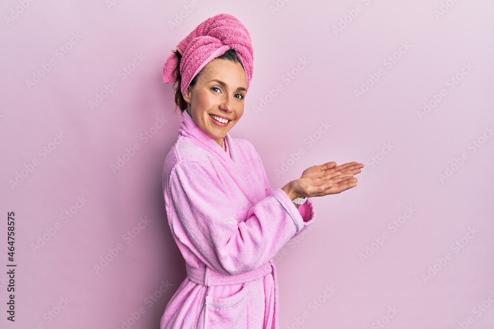 Young blonde woman wearing shower towel cap and bathrobe pointing aside with hands open palms showing copy space, presenting advertisement smiling excited happy Young blonde woman wearing shower towel cap and bathrobe pointing aside with hands open palms showing copy space, presenting advertisement smiling excited happy