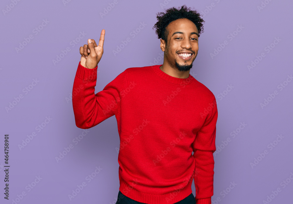 Young african american man with beard wearing casual winter sweater pointing finger up with successful idea. exited and happy. number one. Young african american man with beard wearing casual winter sweater pointing finger up with successful idea. exited and happy. number one.