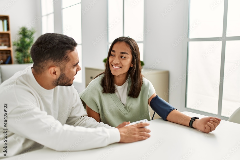 Young latin couple smiling happy measuring blood pressure using tensiometer at home. Young latin couple smiling happy measuring blood pressure using tensiometer at home.