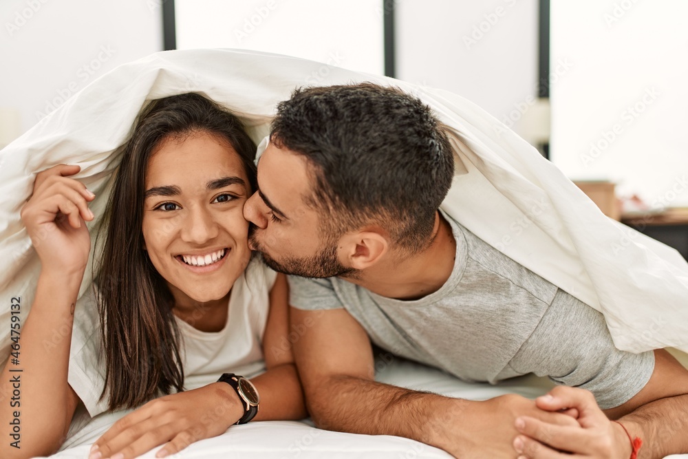 Young latin couple kissing and covering with bed sheet lying on the bed. Young latin couple kissing and covering with bed sheet lying on the bed.