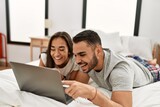 Young latin couple smiling happy using laptop lying on the bed.