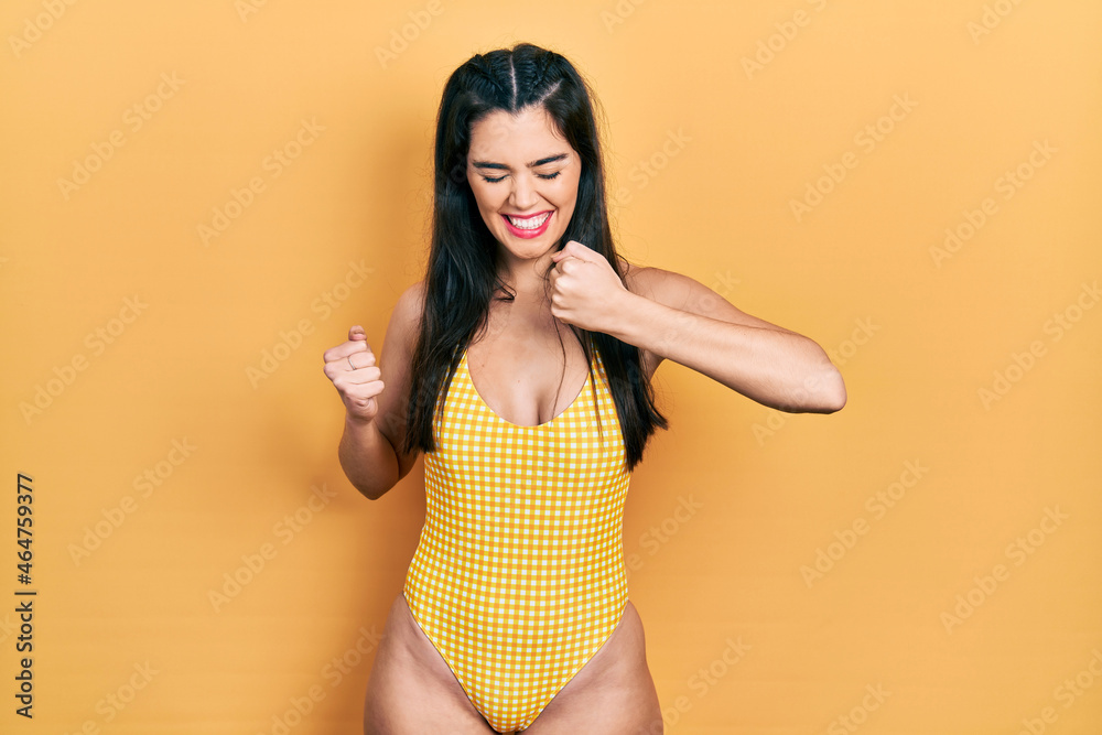 Young hispanic girl wearing swimsuit celebrating surprised and amazed for success with arms raised and eyes closed. winner concept.