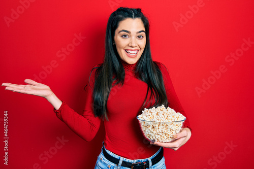 Young hispanic girl eating popcorn celebrating achievement with happy smile and winner expression with raised hand