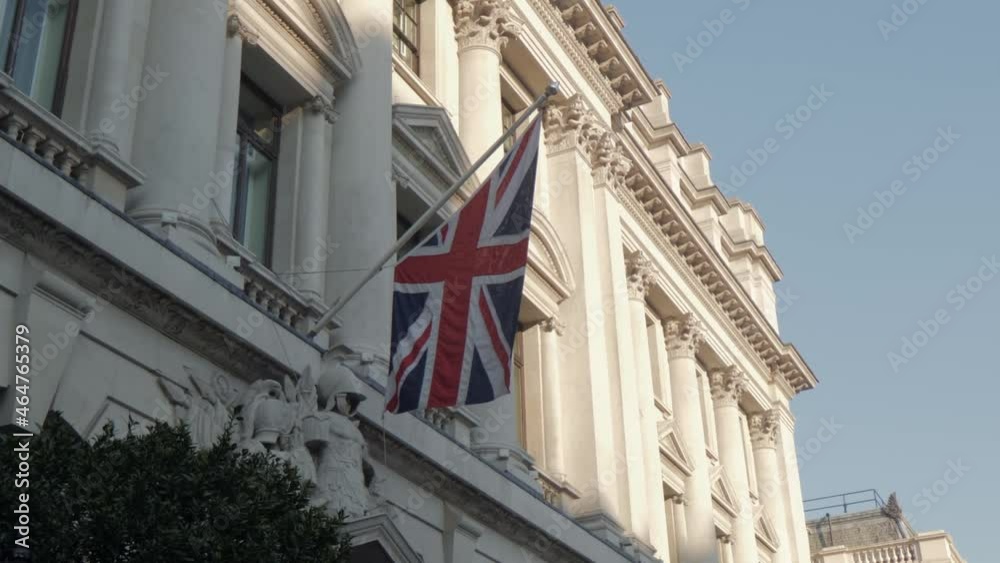 Union Jack flag hanging in front of a white building. Facade of a house in England during sunset. Sunlight in the evening shining on architecture. Union Jack flag hanging in front of a white building. Facade of a house in England during sunset. Sunlight in the evening shining on architecture.