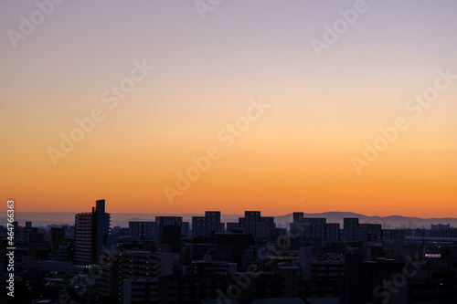 都市の夜明け、早朝ビルの隙間から太陽が昇り辺りはオレンジ色に染まる。ビルはシルエットに浮かぶ © 宮岸孝守