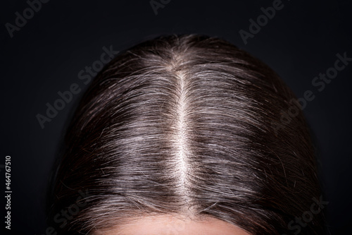 Womens head with gray hair, close-up view of regrown roots, top view on dark background.