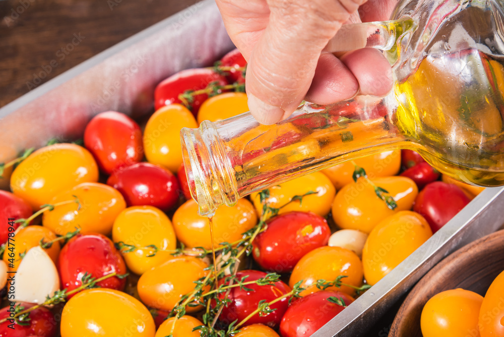 Cooking tomato confit, a woman pours oils into a baking sheet with colorful tomatoes, an elderly