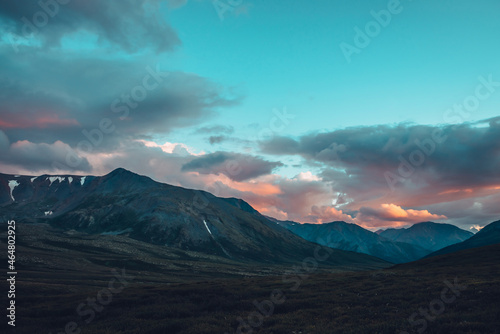 Beautiful surreal mountain scenery with dawn light in cloudy sky. Scenic mountain landscape with surrealist colors in sunset sky. Fantasy silhouettes of mountains on sunrise. Surreal sunlight in sky.