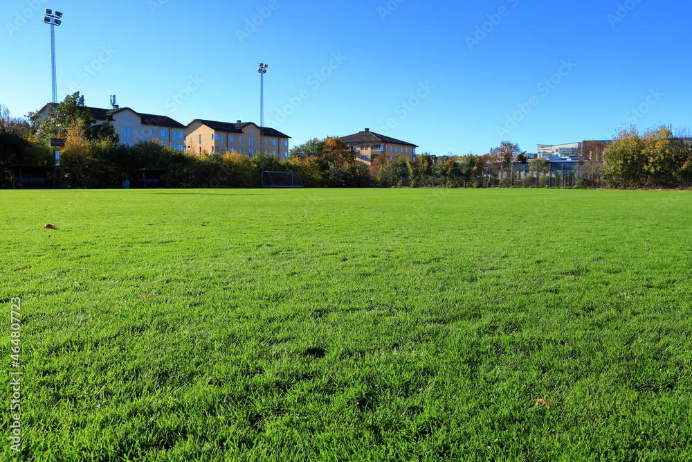 Very green grass at a soccer field. Residential living with apartments in the background. Clear blue sky. Stockholm, Sweden. Very green grass at a soccer field. Residential living with apartments in the background. Clear blue sky. Stockholm, Sweden.