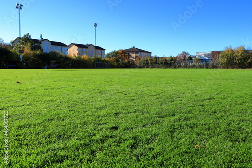 Very green grass at a soccer field. Residential living with apartments in the background. Clear blue sky. Stockholm, Sweden.