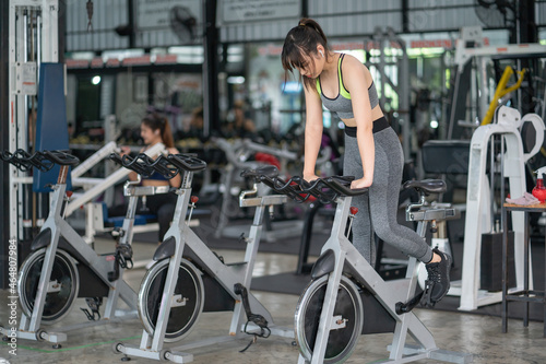 Beautiful Asian woman exercising on stationary cycling machine in indoor fitness gym